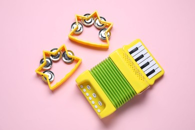 Photo of Bright toy tambourines and accordion on pink background, flat lay