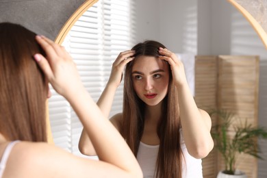 Beautiful woman with healthy hair roots near mirror at home