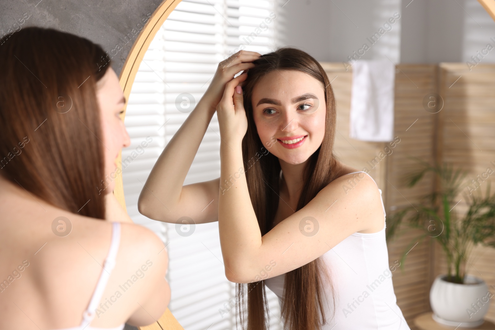 Photo of Smiling woman with healthy hair roots near mirror at home