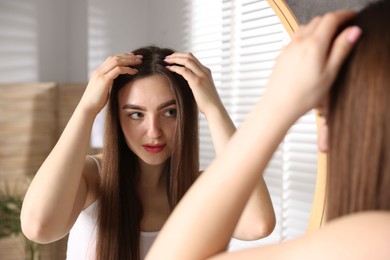 Photo of Beautiful woman with healthy hair roots near mirror at home