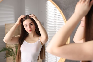 Photo of Beautiful woman with healthy hair roots near mirror at home