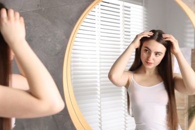 Beautiful woman with healthy hair roots near mirror at home