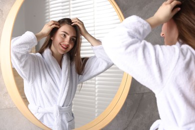 Smiling woman with healthy hair roots near mirror at home