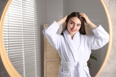 Smiling woman with healthy hair roots near mirror at home