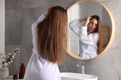 Beautiful woman with healthy hair roots near mirror in bathroom