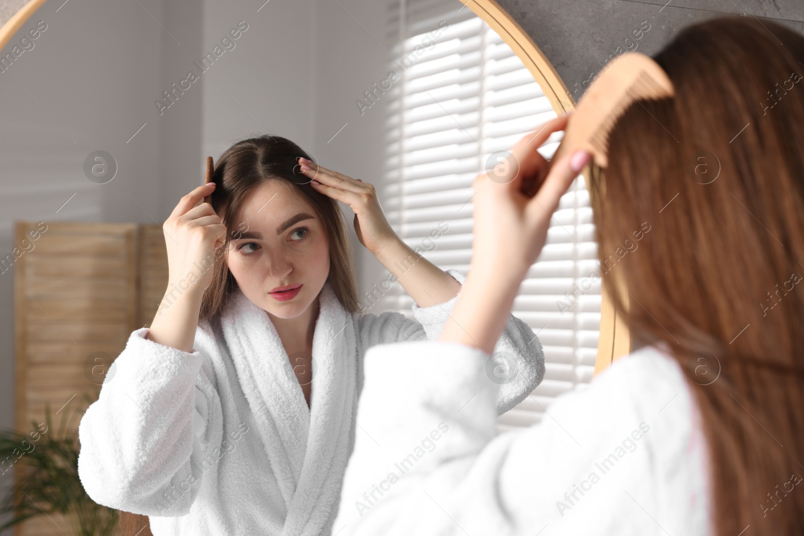 Photo of Beautiful woman combing her hair with healthy roots near mirror at home