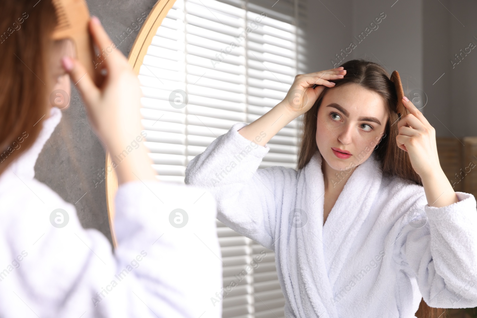 Photo of Beautiful woman combing her hair with healthy roots near mirror at home