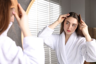 Beautiful woman combing her hair with healthy roots near mirror at home