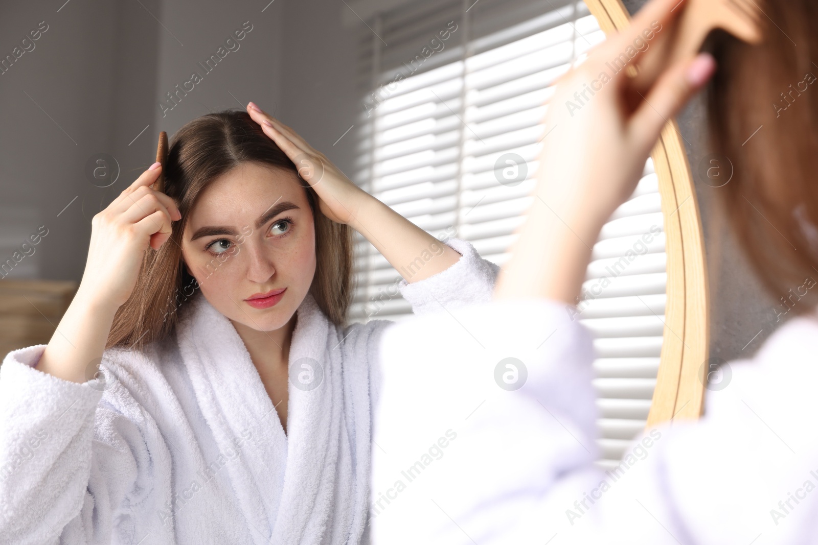 Photo of Beautiful woman combing her hair with healthy roots near mirror at home