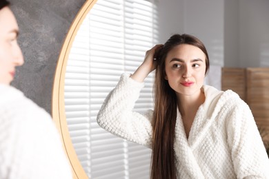 Beautiful woman with healthy hair roots near mirror at home