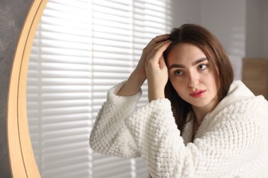 Beautiful woman with healthy hair roots near mirror at home