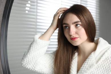 Beautiful woman with healthy hair roots near mirror at home