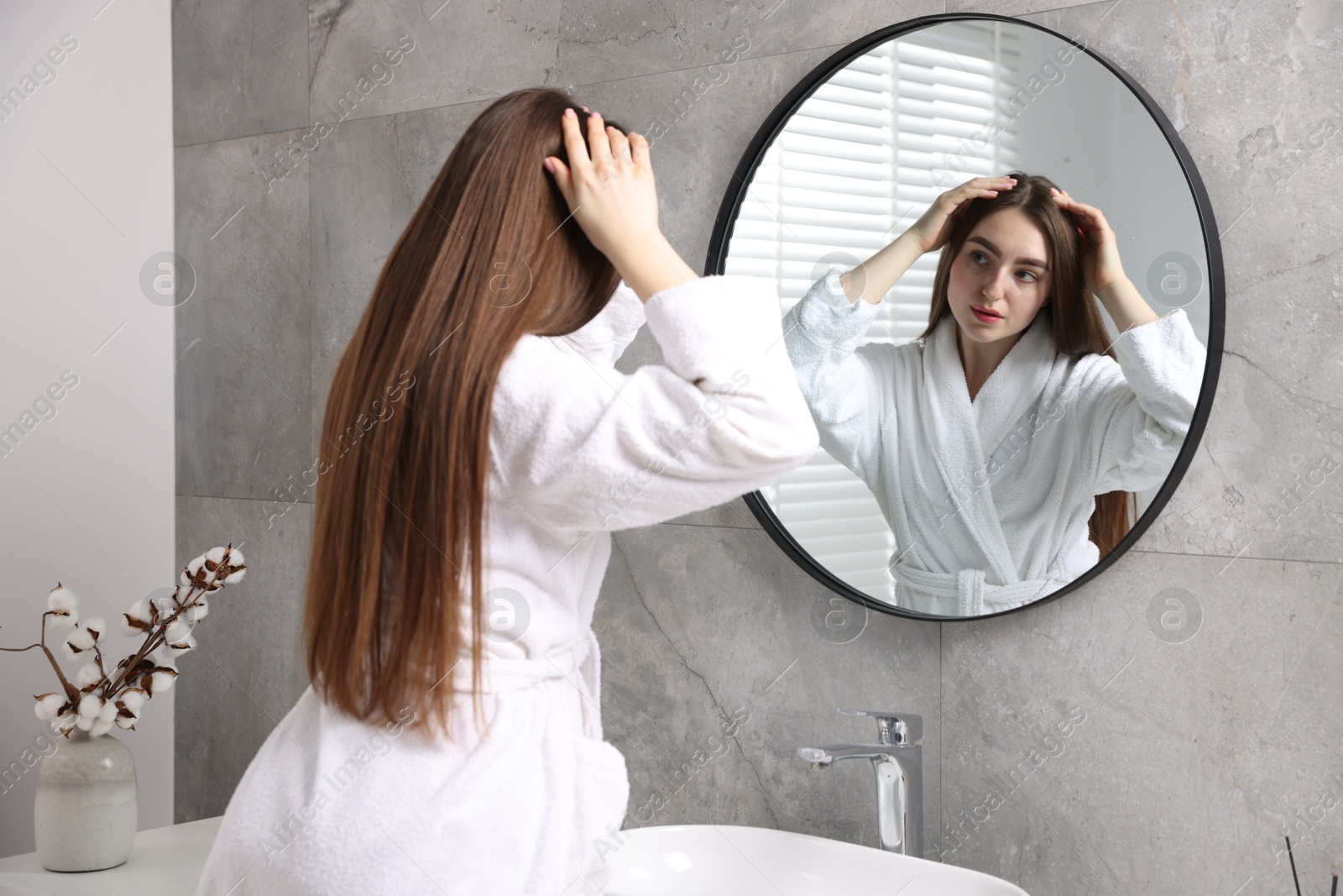 Photo of Beautiful woman with healthy hair roots near mirror in bathroom