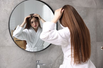 Beautiful woman with healthy hair roots near mirror at home