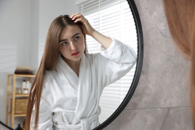 Beautiful woman with healthy hair roots near mirror at home