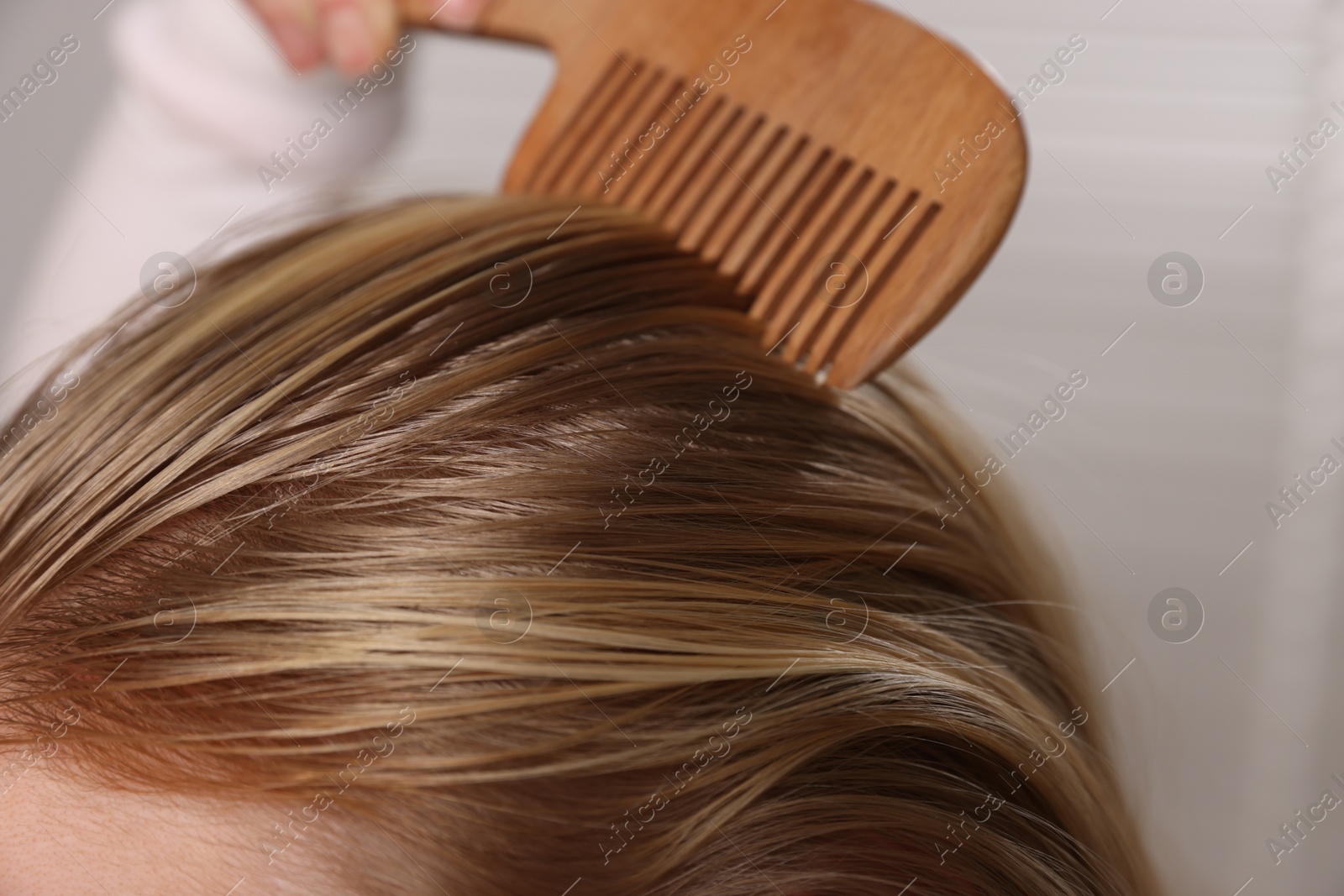 Photo of Woman combing her hair with undying roots on blurred background, closeup