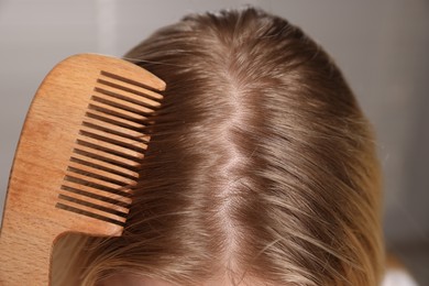 Woman combing her hair with undying roots on blurred background, closeup