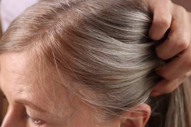 Senior woman with healthy hair roots on blurred background, closeup