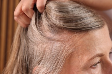 Senior woman with healthy hair roots on blurred background, closeup