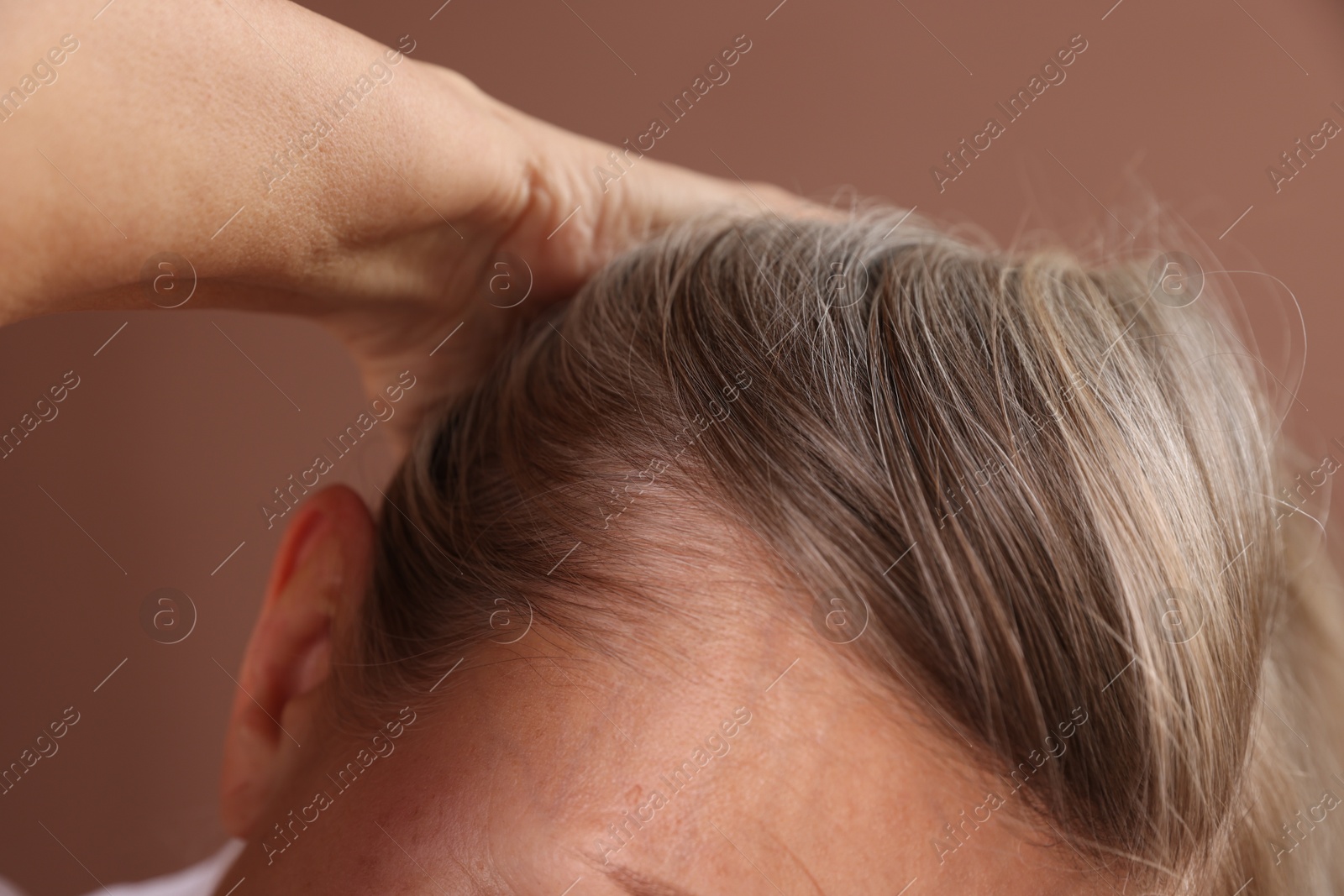 Photo of Senior woman with healthy hair roots on brown background, closeup