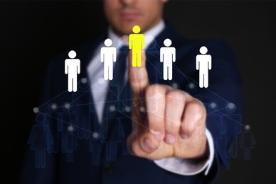 Targeting, recruitment, human resources management. Businessman touching virtual screen with scheme of human icons against black background, closeup