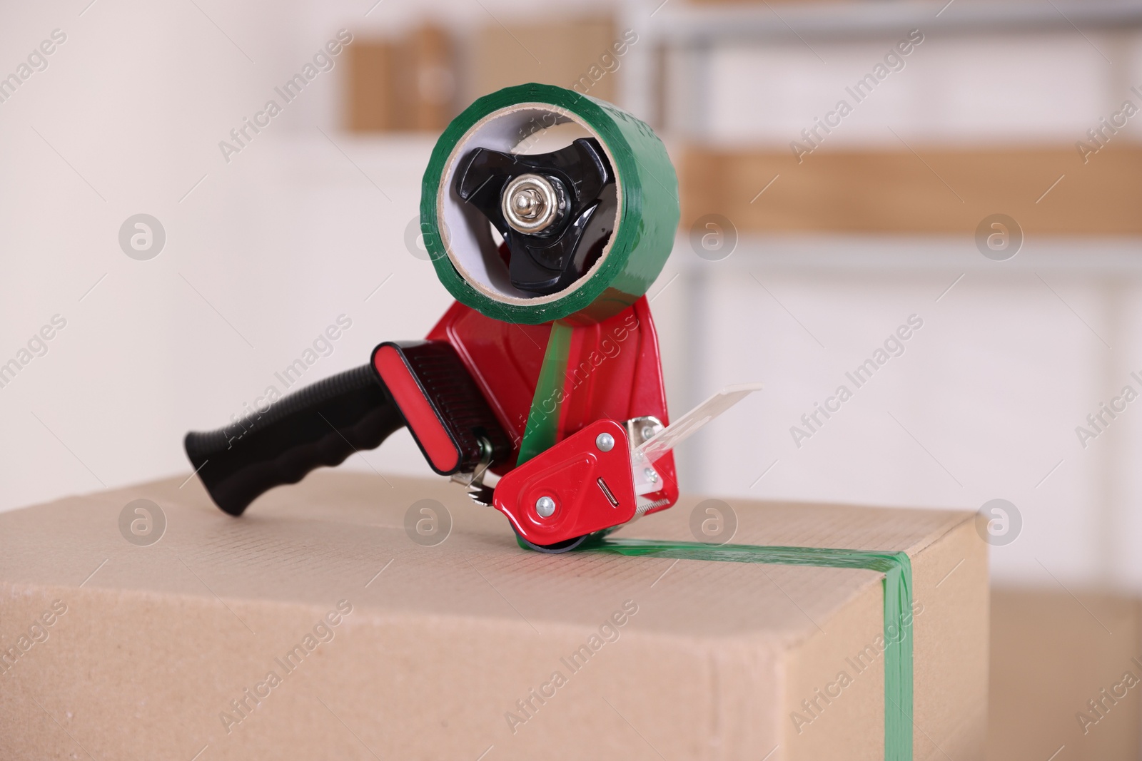 Dispenser with adhesive tape on cardboard box indoors, closeup Photo of Dispenser with adhesive tape on cardboard box indoors, closeup