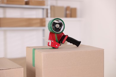 Photo of Dispenser with adhesive tape on cardboard box indoors, closeup