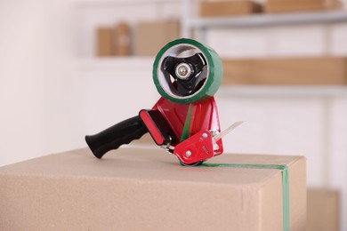 Photo of Dispenser with adhesive tape on cardboard box indoors, closeup