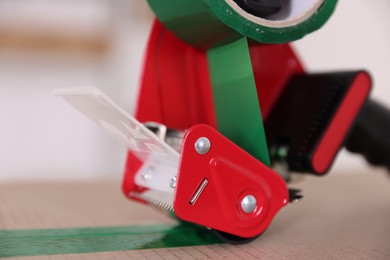 Photo of Dispenser with adhesive tape on cardboard box indoors, closeup