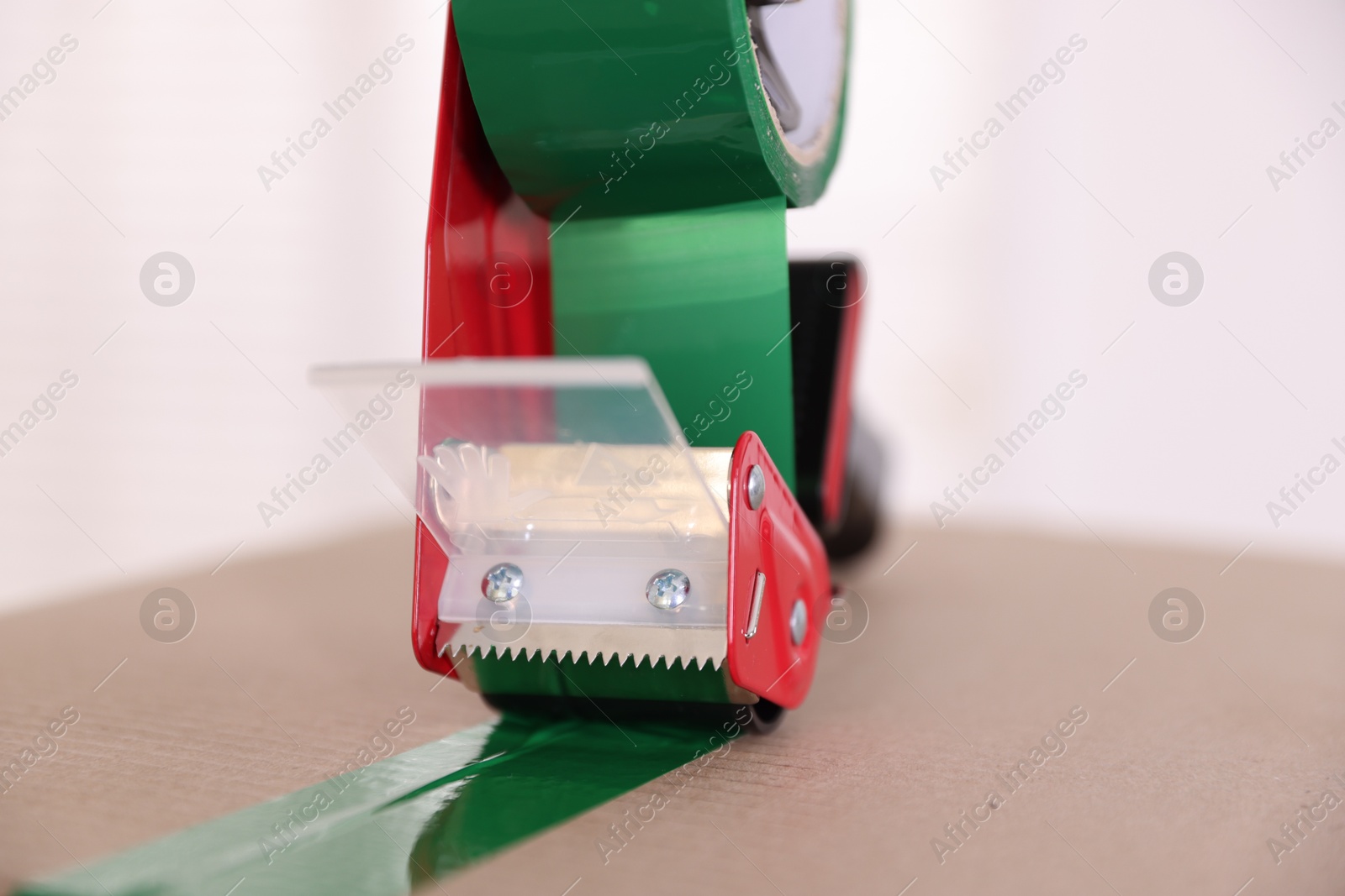Dispenser with adhesive tape on cardboard box indoors, closeup Photo of Dispenser with adhesive tape on cardboard box indoors, closeup