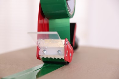 Photo of Dispenser with adhesive tape on cardboard box indoors, closeup