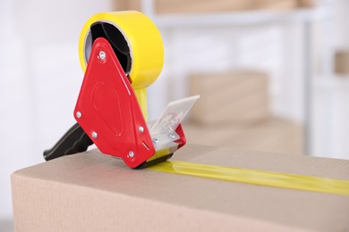 Photo of Dispenser with adhesive tape on cardboard box indoors, closeup. Space for text