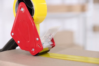 Photo of Dispenser with adhesive tape on cardboard box indoors, closeup. Space for text