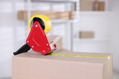 Photo of Dispenser with adhesive tape on cardboard box indoors, closeup. Space for text