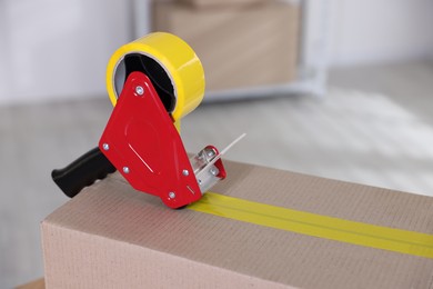 Photo of Dispenser with adhesive tape on cardboard box indoors, closeup. Space for text