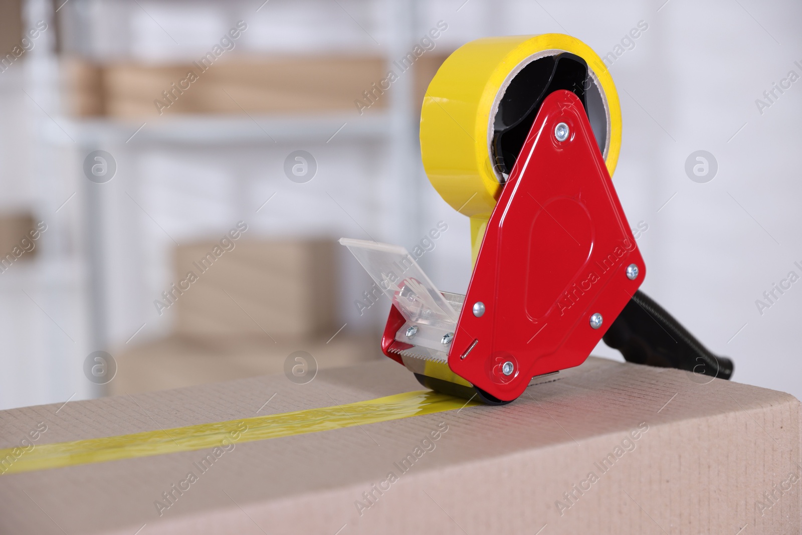 Dispenser with adhesive tape on cardboard box indoors, closeup. Space for text Photo of Dispenser with adhesive tape on cardboard box indoors, closeup. Space for text