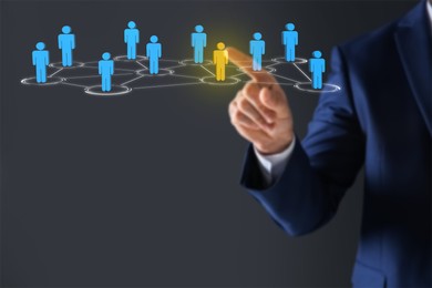 Targeting, recruitment, customer acquisition. Businessman touching virtual screen with scheme of human icons against dark grey background, closeup