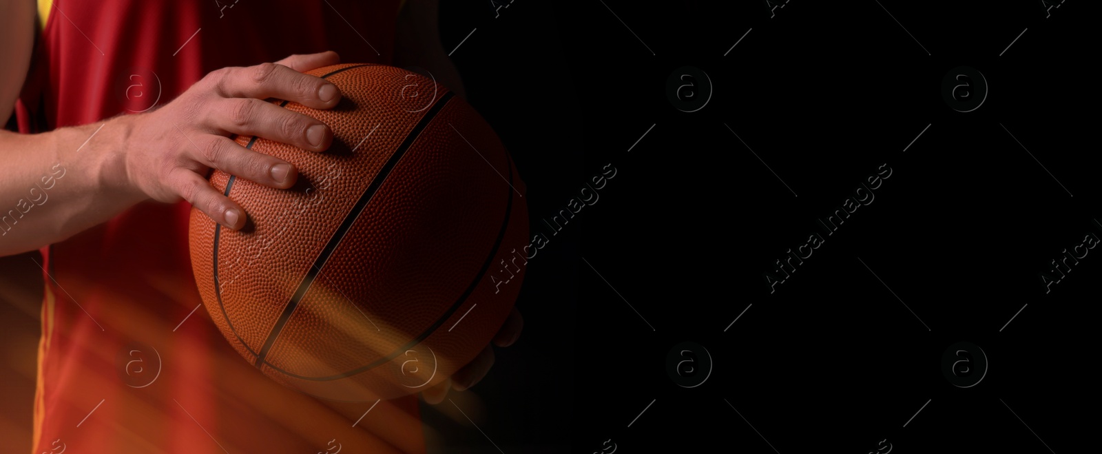 Image of Athletic man with basketball ball in orange lights on black background, closeup. Banner design with space for text. Stylish poster for sportive event