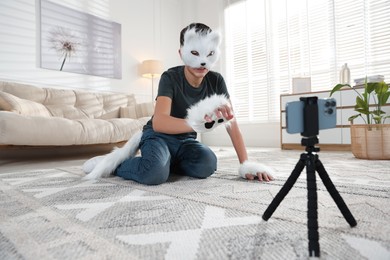 Photo of Quadrobics. Boy in cat mask, gloves and tail recording video at home