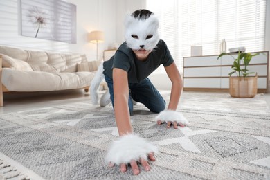 Photo of Quadrobics. Boy wearing cat mask, gloves and tail on floor at home