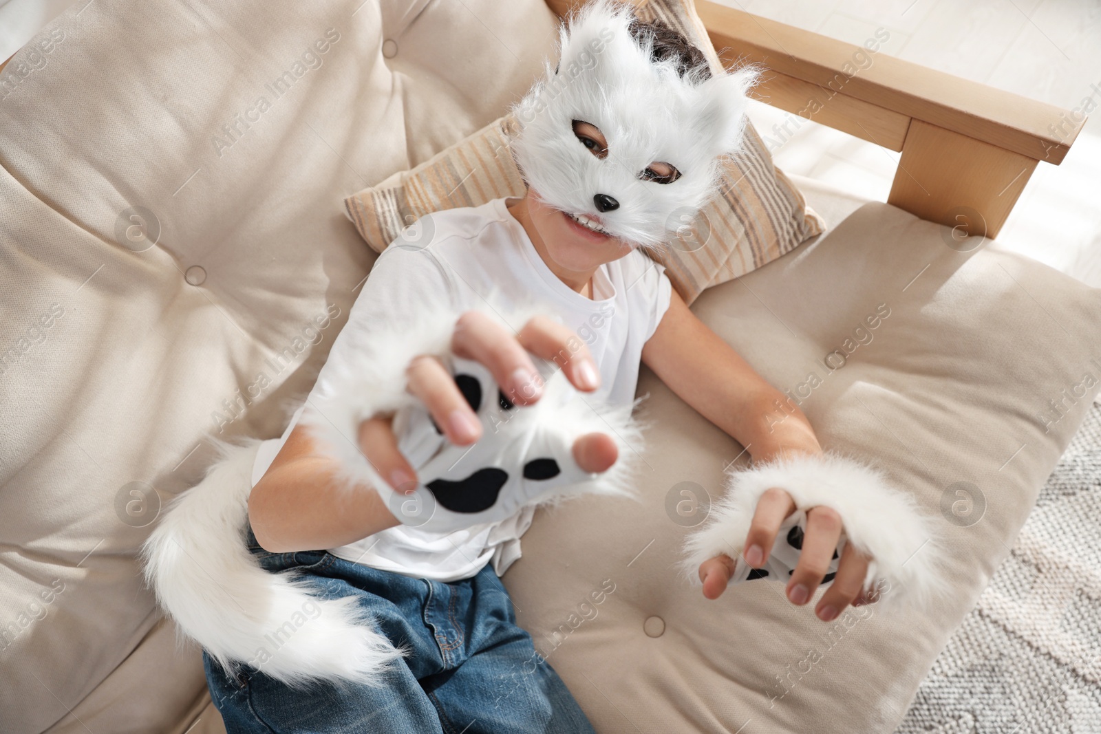 Photo of Quadrobics. Boy wearing cat mask, gloves and tail on sofa at home, above view