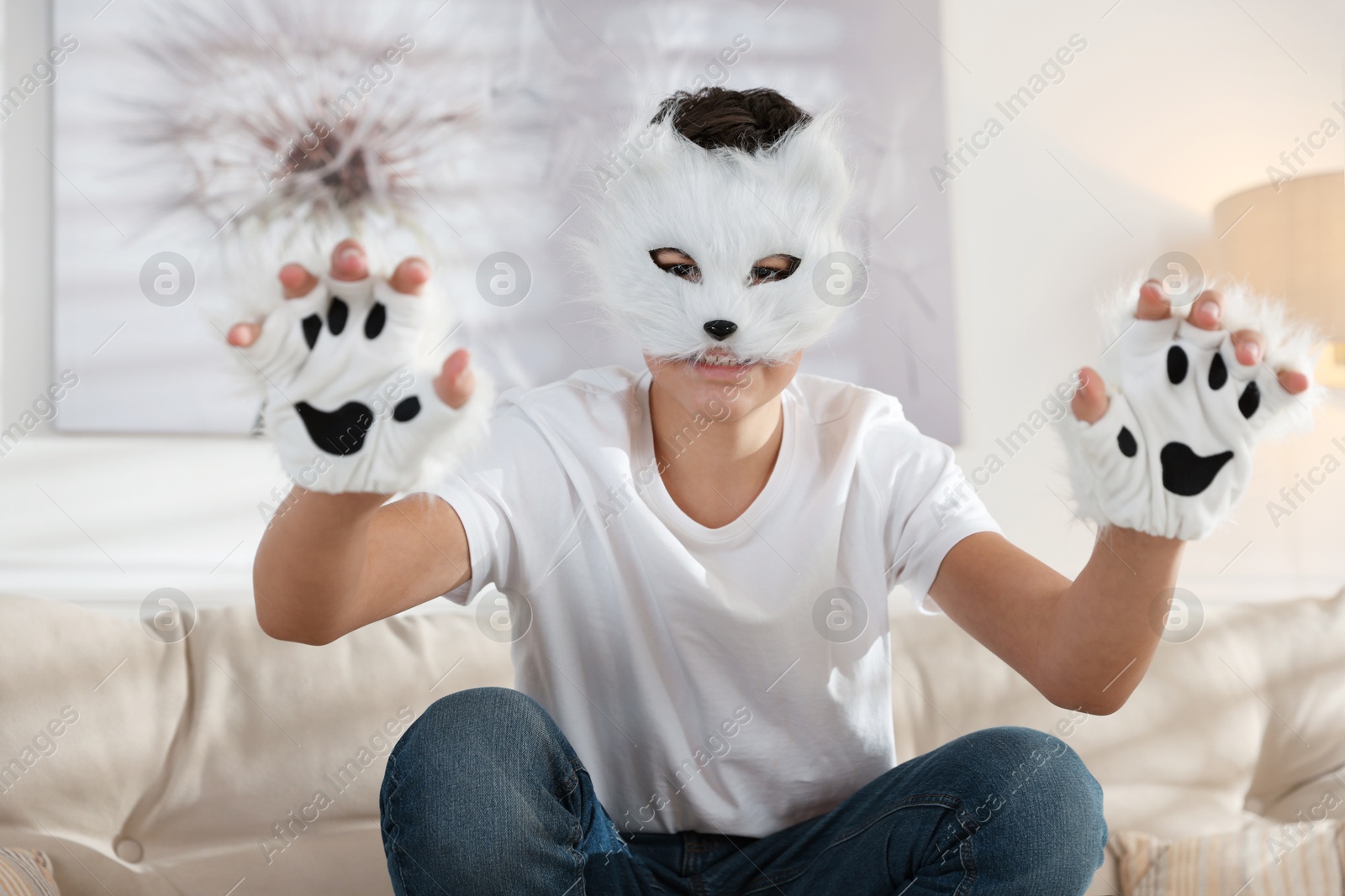 Photo of Quadrobics. Boy wearing cat mask and gloves on sofa at home