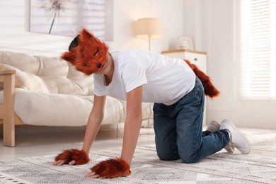 Photo of Quadrobics. Boy wearing fox mask, gloves and tail on floor at home