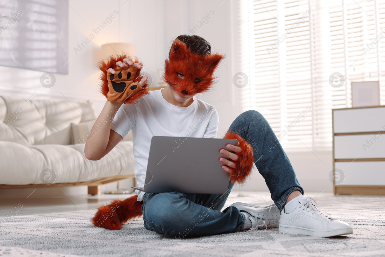 Photo of Quadrobics. Boy in fox mask, gloves and tail holding laptop at home