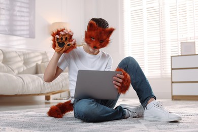 Quadrobics. Boy in fox mask, gloves and tail holding laptop at home