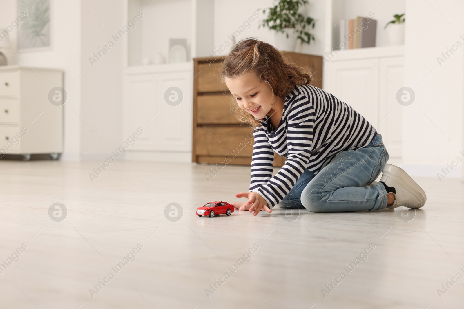 Photo of Little girl playing with toy car on floor at home, space for text