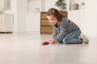 Little girl playing with toy car on floor at home, space for text