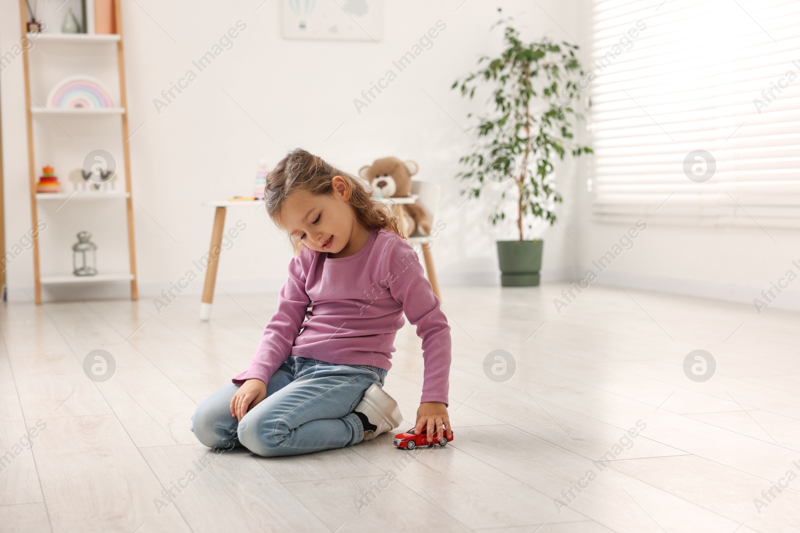 Photo of Little girl playing with toy car on floor at home