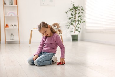 Little girl playing with toy car on floor at home