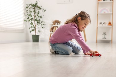 Little girl playing with toy car on floor at home, space for text